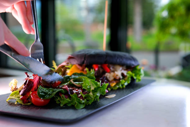 bulgogi, spicy bulgogi, house-made, squid inc bread, beef black bread bun with cuttlefish ink sandwich hamburger restaurant serving with salad on a black plate near the window delicious appetizing