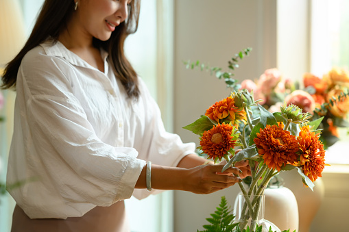 Smiling young woman florist in white shirt arranging flowers in vase. Small business and floristry concept.