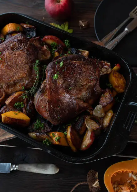 Delicious homemade meat dish or with oven roasted turkey shanks. Served with butternut squash, apples and onions in a roasting pan isolated on wooden table background with autumn decoration for thanksgiving.