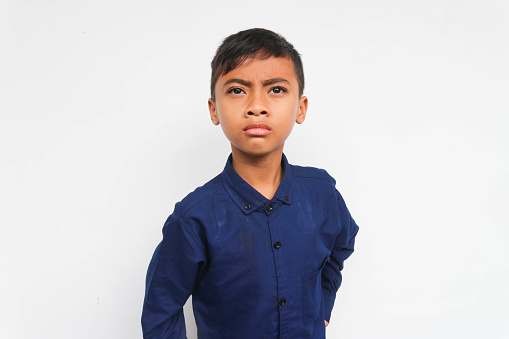 Angry boy wearing a blue shirt looking at the camera with serious face. Isolated on white background