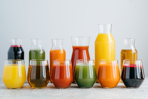 Multicolored fruit juice in glass jars isolated over white background. Drinks containing vitamins made of orange, pomegranate, carrot, spinach