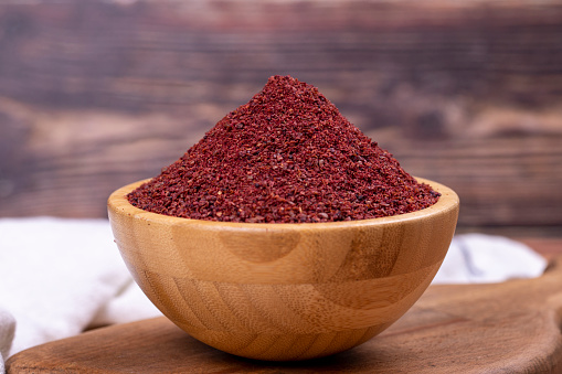 Sumac on wooden background. Dried ground red Sumac powder spices in wooden bowl. Close up