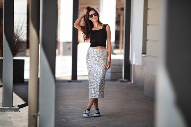Fashionable woman wears shiny maxi skirt with sequins, black sneakers and Tshirt. Fashion street style clothing. Adult female model with long dark hair stock photo