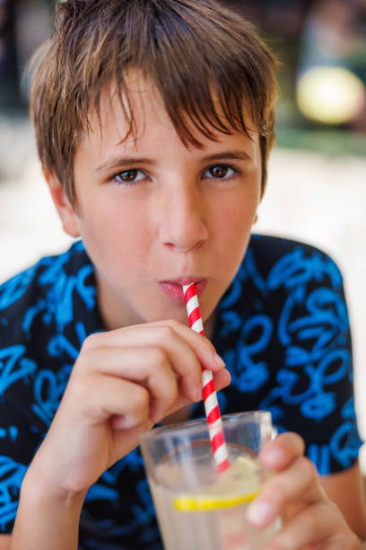 istock Preadolescent boy drinking cold lemonade on red and white paper straw and looking at camera 1489381901