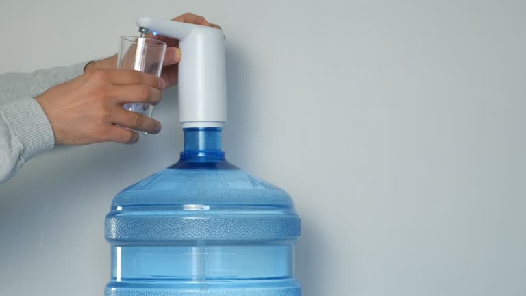 Man's hands pour water into glass from an automatic water cooler, closeup view.