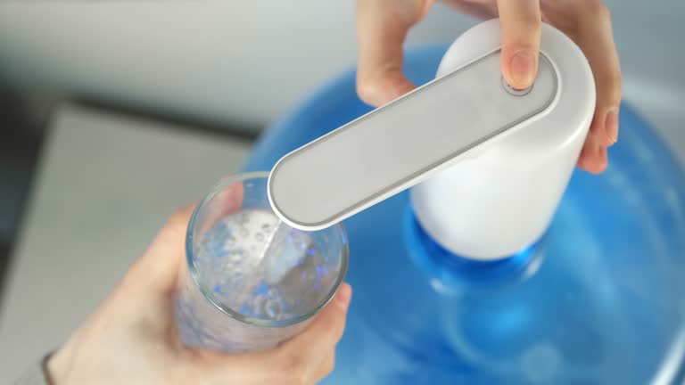 Woman's hands pour water into glass from automatic water cooler, closeup view.