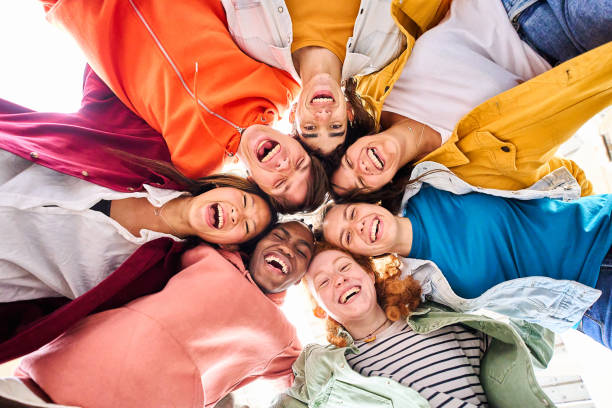 istock Large multiracial group of smiling young people standing hugging looking at camera. Low angle view. 1489384301