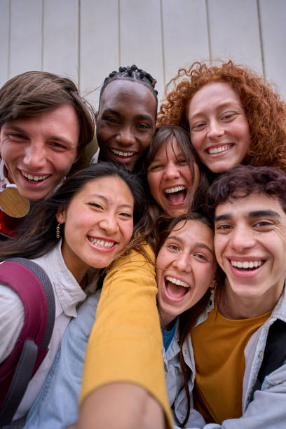 Vertical phone selfie of excited multiracial group of erasmus college students together outside. stock photo