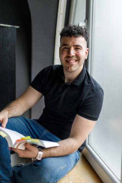 istock Young male university student sitting on the window sill and studying 1489388035