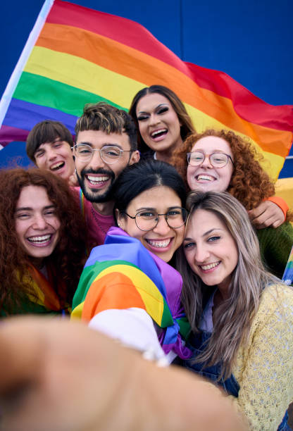 Vertical selfie of LGBT group young people celebrating gay pride day holding rainbow flag together Vertical selfie of LGBT group of young people celebrating gay pride day holding rainbow flag together. Homosexual community smiling taking cheerful self portrait. Lesbian couple friends generation z. lesbian pride stock pictures, royalty-free photos & images