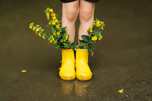 Cute little baby boy walks through puddles on a spring day, wearing raincoat and rubber boots. Happy and joyful child in colorful yellow coat fashion casual clothes