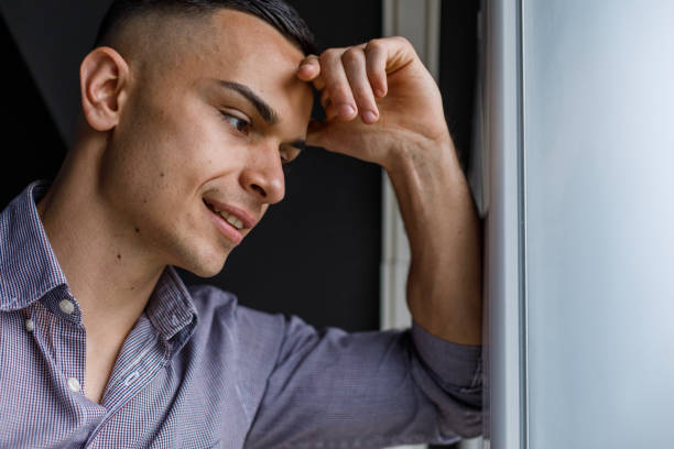 istock Happy young man leaning against the window, looking outside, contemplating 1489391036