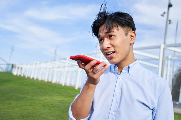 istock Asian boy using mobile in city park. Chinese guy sending a voicemail message on cell phone outdoors 1489391948