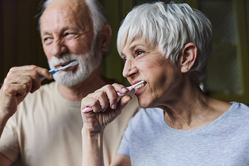 Mature woman and her husband brushing their teeth during morning routine.