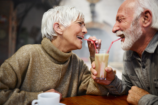 Cheerful mature couple having fun while drinking lemonade from the same glass in a café.