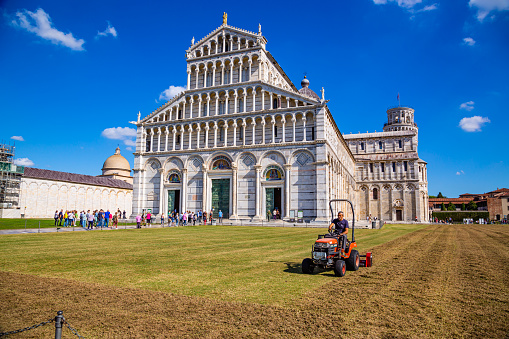 Pisa,Tuscany,Italy 5 october 2022:Many tourists visit the basilica while an employee mows the lawn in Piazza dei Miracoli