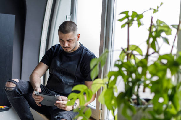 istock Young man sitting on the window sill, relaxing and using digital tablet 1489393969