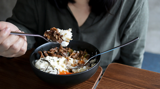 A person eating a meal holding a spoon of rice and meat from a black bowl of rice meat.