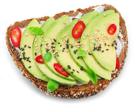 Avocado toast - bread with avocado slices, pieces of chilli pepper and black sesame isolated on white background. Top view.