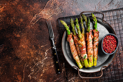 Baked Prosciutto wrapped green asparagus. Dark background. Top view. Copy space.