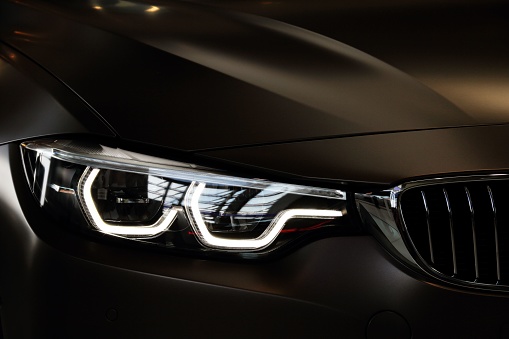 Munich, Germany – May 10, 2018: A BMW car headlight illuminated against a black background.