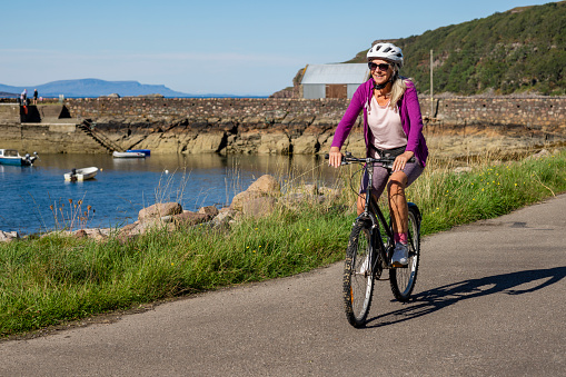 Senior woman on a bike ride at the bay near the village of Diabaig on the side of Loch Torridon in Wester Ross, Scotland. She is taking a break from the ride to relax.