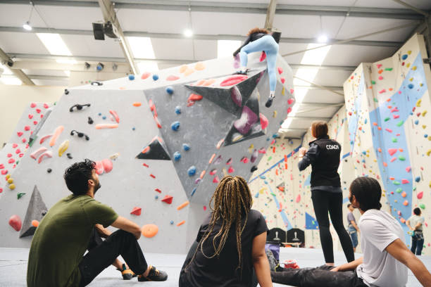 istock Multi-Cultural Group Watching Friend On Climbing Wall In Indoor Activity Centre With Coach 1489402277