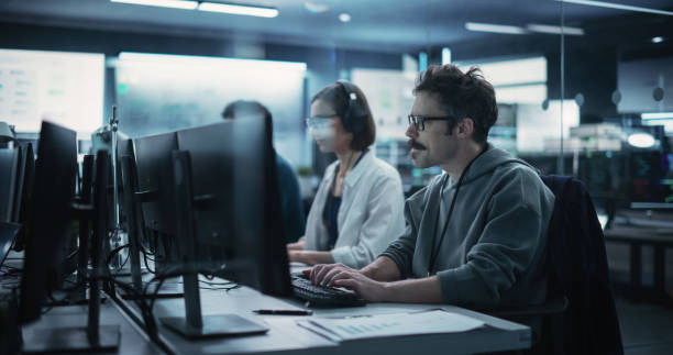 istock Diverse Young Colleagues Working on Computers in a Research Laboratory. Female Asking Advice from a Male Software Developer Colleague About a Solution for Their Collaborative Industrial Tech Project 1489403479
