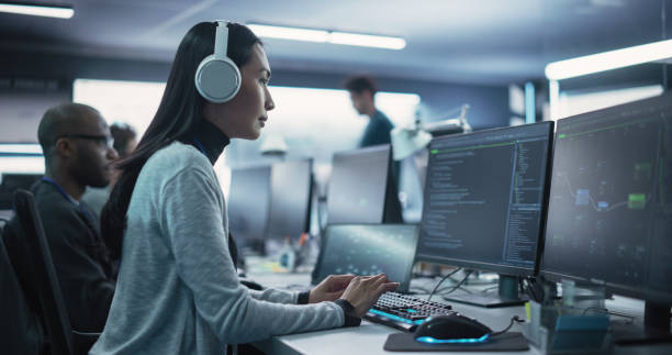 istock Portrait of a Thoughtful Young Engineer Working on Computer in a Technological Office Environment. Beautiful Asian Woman Wearing Headphones, Writing Software Code for a Blockchain Project 1489403918