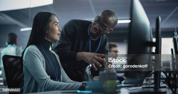 Two Diverse Multiethnic Colleagues Having A Conversation While Busy Working On A Team Project Asian Female Designer Talking With An African Project Manager Teamwork In Technology Laboratory Stock Photo - Download Image Now