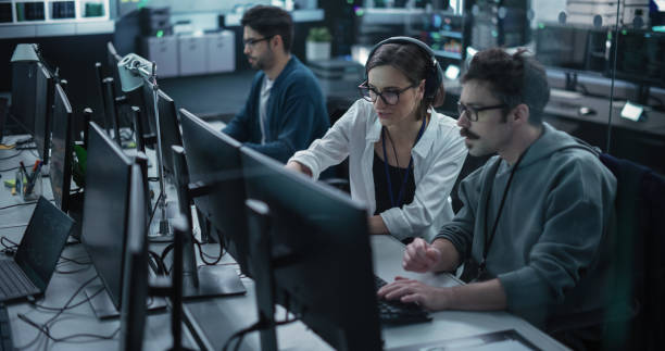 istock Young Team of Specialists Working on Desktop Computers and Having a Conversation at a Workplace. Female and Male Software Developers Discussing a Solution for Their Artificial Intelligence Project 1489405359