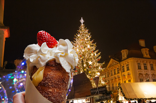 Trdelnik, typical Czech dessert, with cream and strawberry, Old Town Square in Prague. Christmas period.