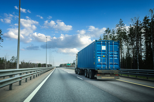 Truck with blue shipping container rides at multiple lane highway at sunset