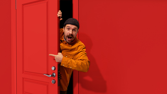 Extremely happy man with moustaches peeking out red door and pointing with positive excitement. Sales, job fair, betting, win, success. Concept of emotions, facial expression, lifestyle