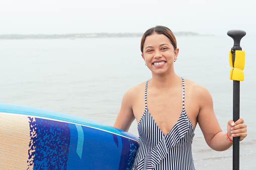 Young Woman standing next to her paddle board by the ocean