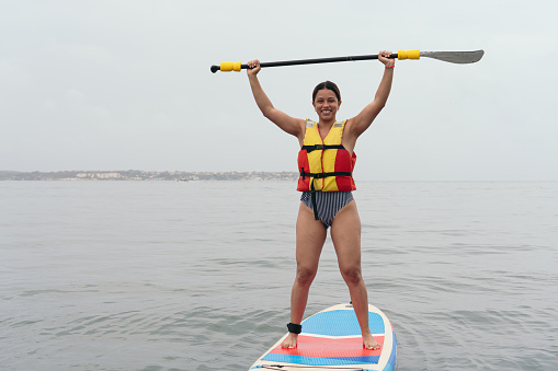 Young Woman in bikini standing on a SUP board training in the sea