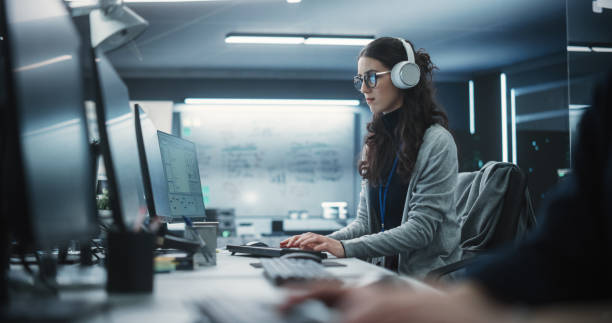istock Portrait of a Thoughtful Young Engineer Working on Computer in a Technological Office Environment. Beautiful Multiethnic Woman Wearing Headphones, Writing Software Code for a Blockchain Project 1489413882