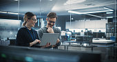 Portrait of Two Creative Young Female and Male Engineers Using Laptop Computer to Analyze and Discuss How to Proceed with the Artificial Intelligence Software. Standing in High Tech Research Office