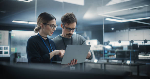 istock Portrait of Two Creative Young Female and Male Engineers Using Laptop Computer to Analyze and Discuss How to Proceed with the Artificial Intelligence Software. Standing in High Tech Research Office 1489414101