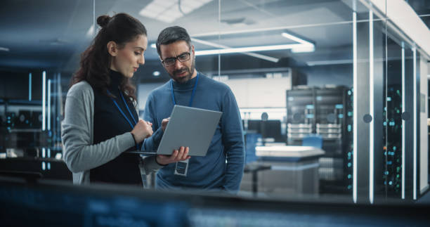 retrato de duas mulheres e homens engenheiros usando computador portátil para analisar e discutir como proceder com o software de inteligência artificial. conversando casualmente no high tech research office - segurança de rede - fotografias e filmes do acervo
