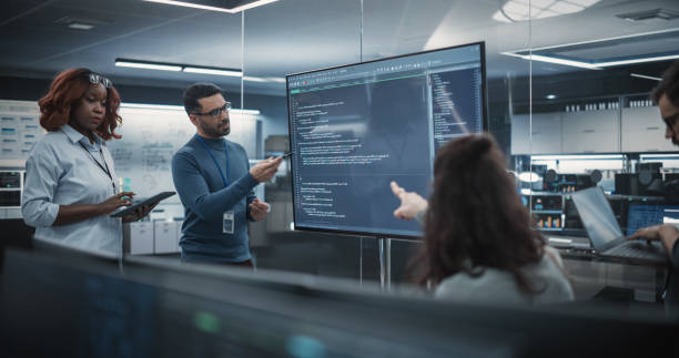 istock Team of Diverse Software Developers Having a Meeting in Order to Review the Code Done by Computer Engineering Department. Manager Making a Presentation for Project Managers at the Office 1489414534