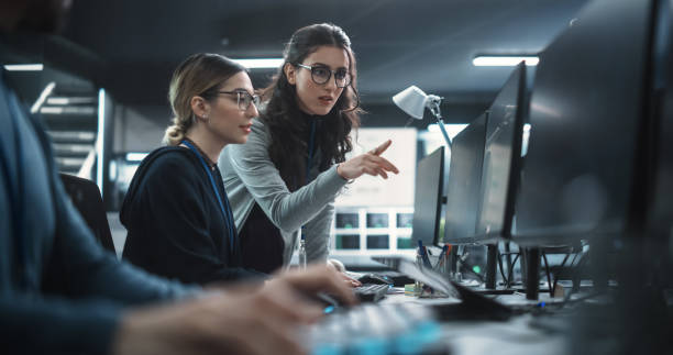 duas belas mulheres trabalhando em um departamento de desenvolvimento de software de segurança cibernética. jovem gerente atualizando desenvolvedor de software no projeto de segurança em inteligência artificial - data center computer programmer women - fotografias e filmes do acervo