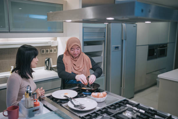 femme malaise asiatique atteinte de vitiligo à la cuisine préparant le petit-déjeuner et parlant à son amie - break eggs domestic kitchen breaking photos et images de collection