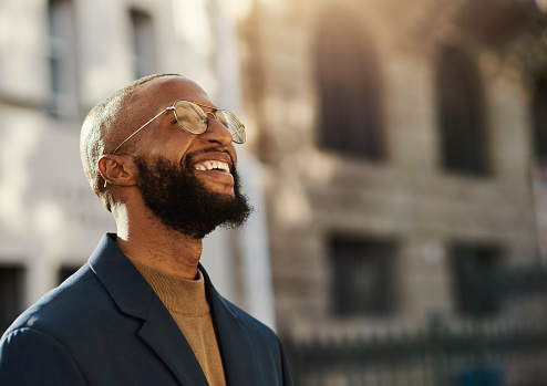 Outdoor portrait of ambitious black business man wearing eye glasses looking up whilst smiling in the city. Stock Photo