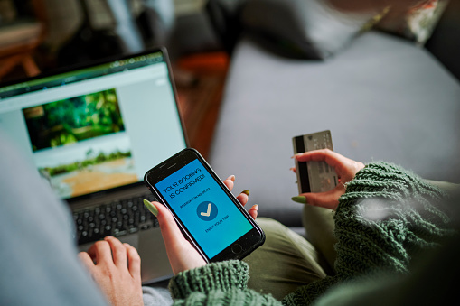 Point of view of female making online booking on a mobile phone. Using laptop and credit card