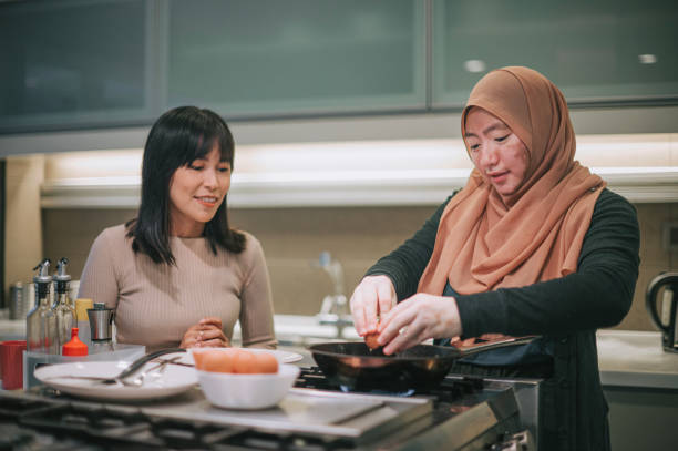 femme malaise asiatique atteinte de vitiligo à la cuisine préparant un œuf au plat et parlant à son amie - break eggs domestic kitchen breaking photos et images de collection