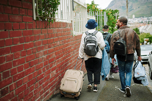 Group of multiracial friends leaving for a road trip. Carrying luggage while walking in a neighborhood. Copyspace