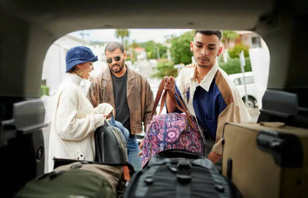 Rear view perspective of a group of LGBTQIA friends packing a car with lugguage before a road trip
