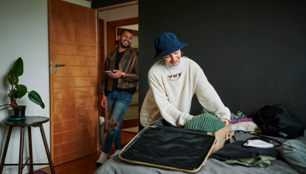 Multiracial non-binary person packing for a trip while talking to flatmate Non-binary person packing clothing into a suitcase for a trip while talking to flatmate flatmate stock pictures, royalty-free photos & images