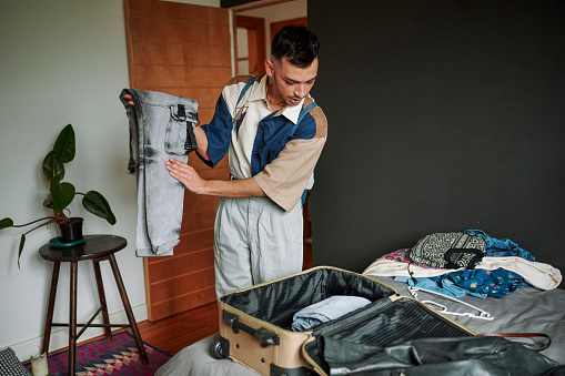 Young man in a bedroom packing and organising clothing for a trip into a suitcase